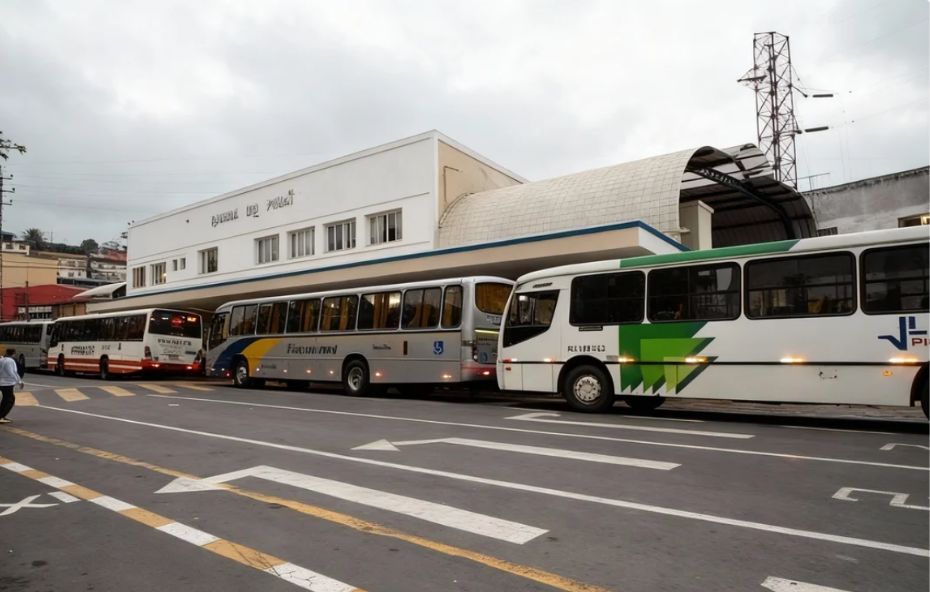 Fotografia da fachada branca do Terminal Rodoviário Roberto Silveira em Barra do Piraí com diversos ônibus coloridos estacionados nas plataformas de embarque sob um céu nublado.