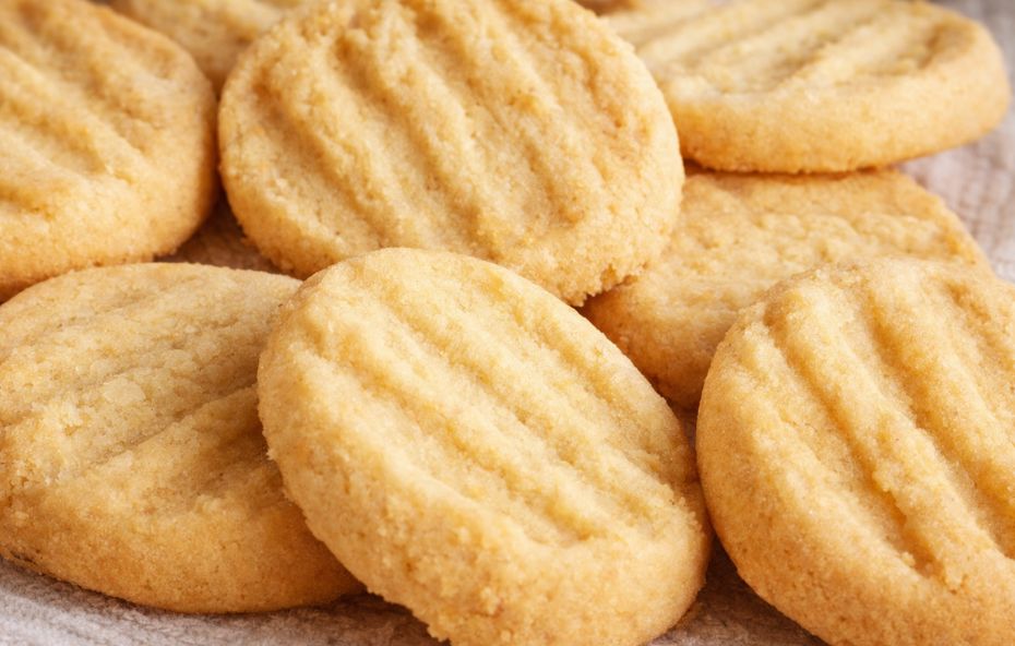 Vários biscoitos amanteigados redondos com marcas de garfo no topo apresentando uma cor dourada suave e textura crocante organizados sobre uma superfície clara.