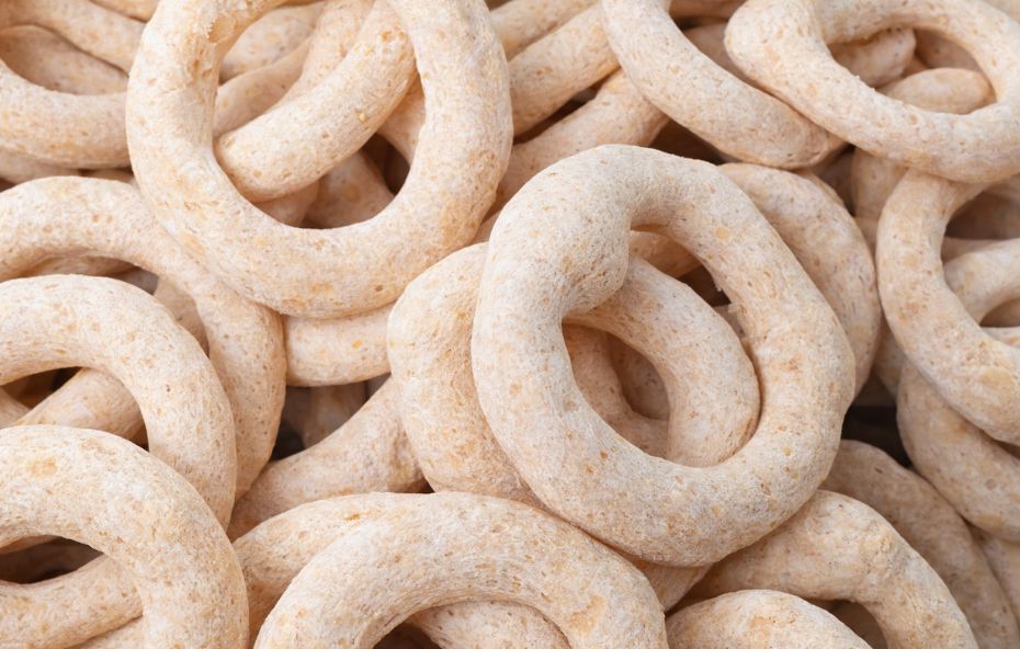 Fotografia em close de diversos biscoitos de polvilho doce circulares com textura porosa e cor bege clara amontoados preenchendo todo o quadro da imagem.