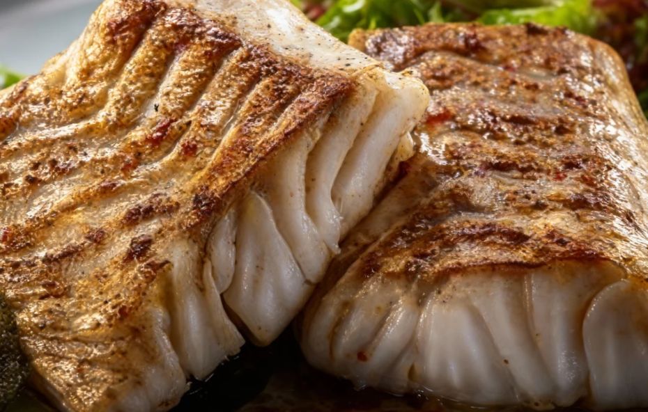 Um refratário de vidro saindo do forno com filés de peixe brancos cobertos por um vinagrete colorido de tomates e pimentões sobre uma camada de batatas douradas.