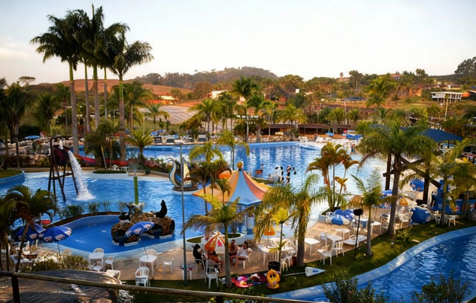 Vista panorâmica de um parque aquático com diversas piscinas azuis cercadas por palmeiras e áreas de descanso com guarda-sóis e mesas em um dia ensolarado.